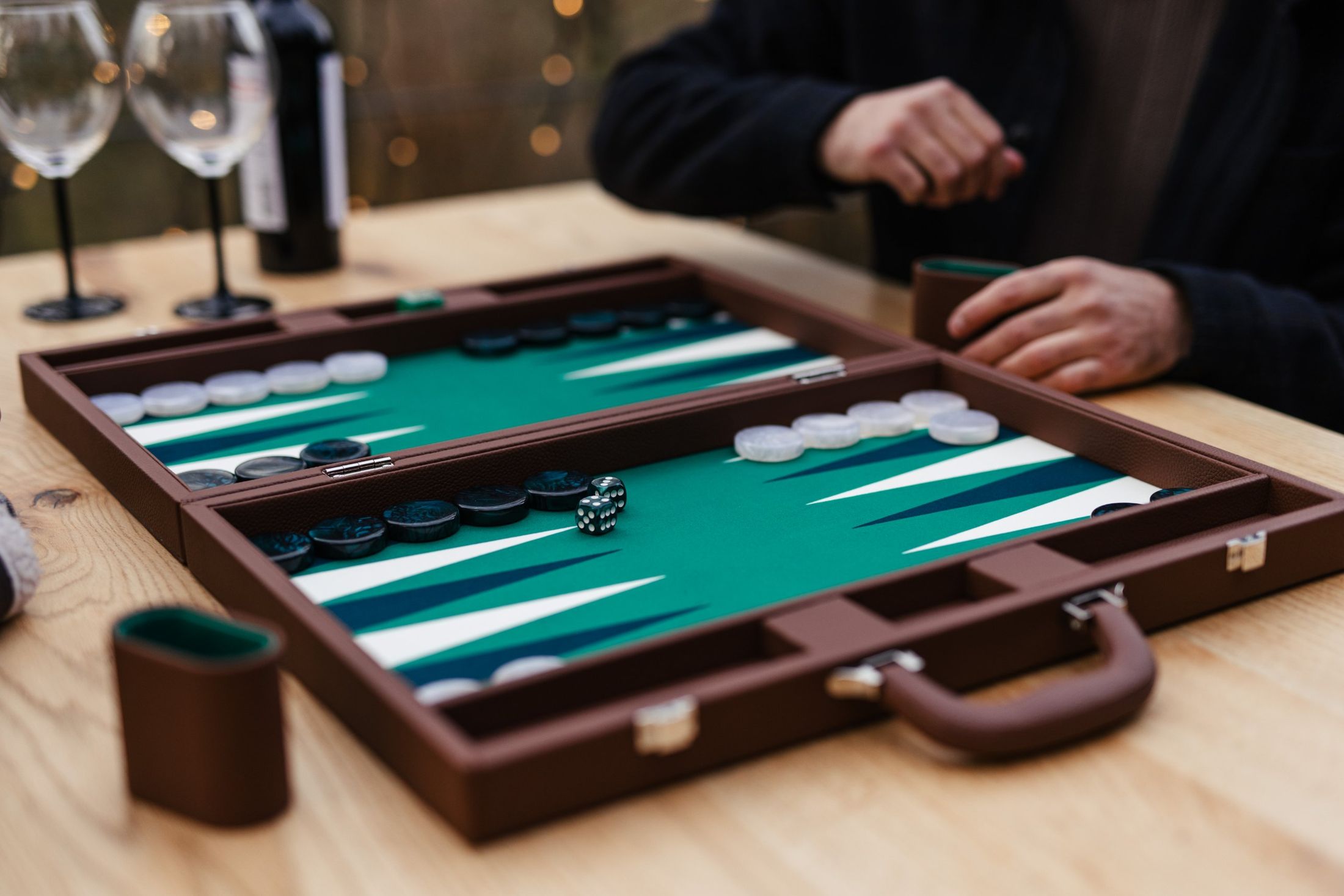 A Pointworks backgammon set mid-game on a timber table, with wine glasses behind