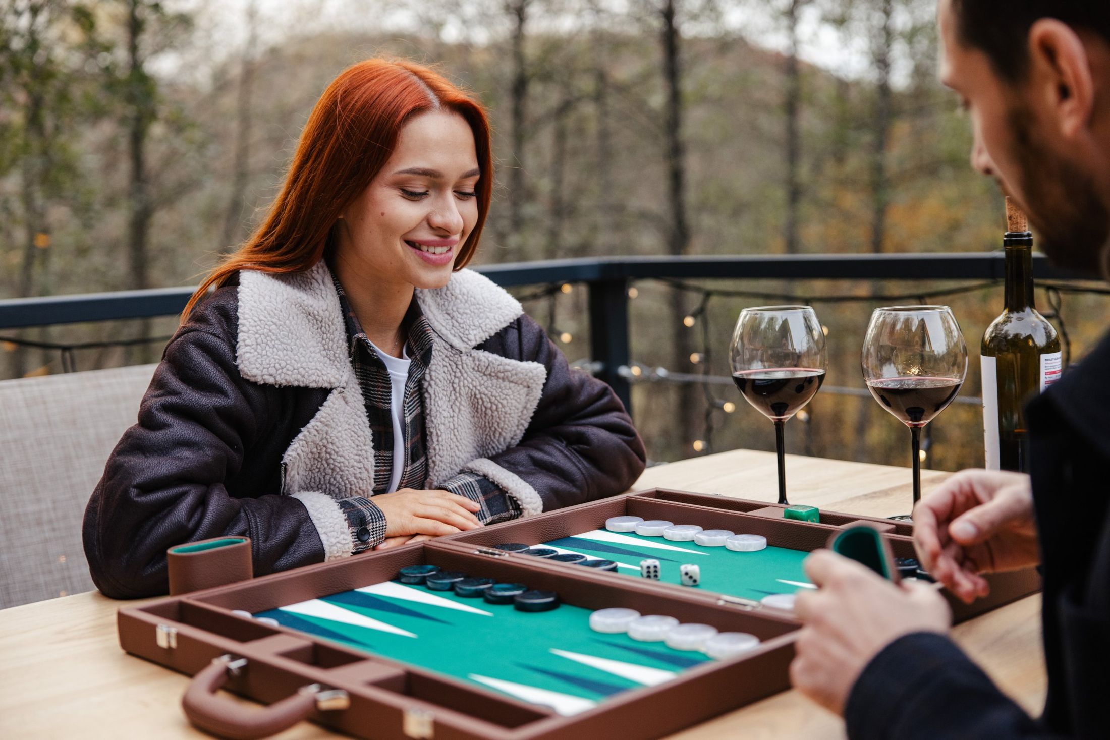 Two people playing a Pointworks backgammon set at a timber table outdoors